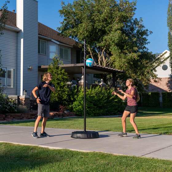 Two players face off outdoors, taking turns striking a Lifetime tetherball tied to a tall sturdy steel pole