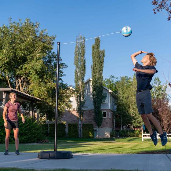 Two players enjoying tetherball with a steel pole, soft ball, and sturdy portable base setup.