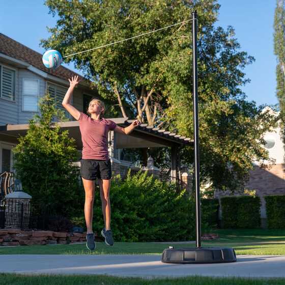 Lady player jumps to hit Lifetime tetherball attached to a tall sturdy steel pole.